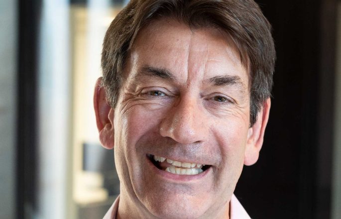 Caucasian man smiling at camera, with brown short hair and wearing a pink shirt