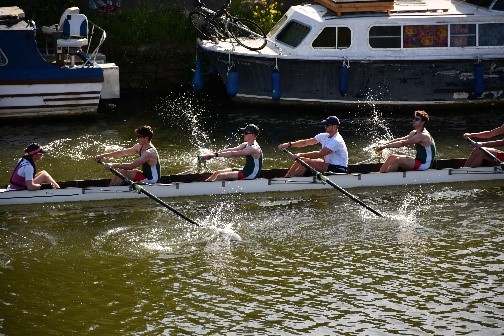 the Jesus College Men's 1 crew rowing in sunshine, blades striking the water