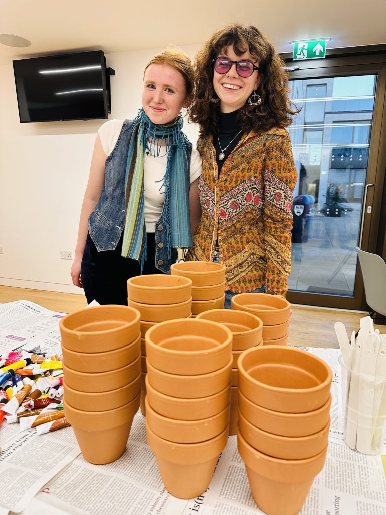 Table covered in flower pots with two young women standing behind smiling and hugging