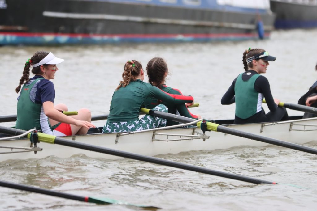 Close up view of Jesus Boat Club women in boat, wearing green tops, oars in water