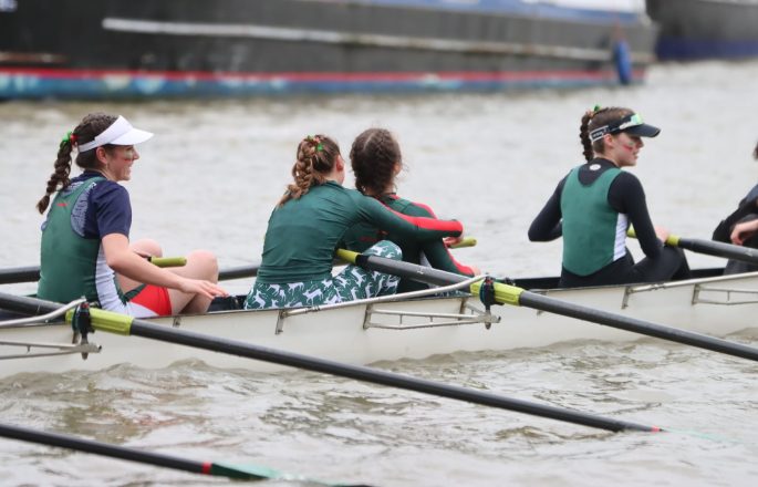Close up view of Jesus Boat Club women in boat, wearing green tops, oars in water