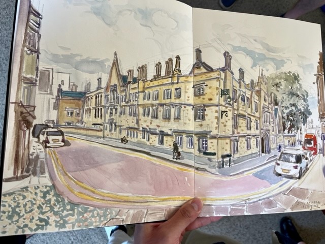 Paint and pencil drawing in sketchbook of building in warm yellow tones. hand of artist holding sketchbook 