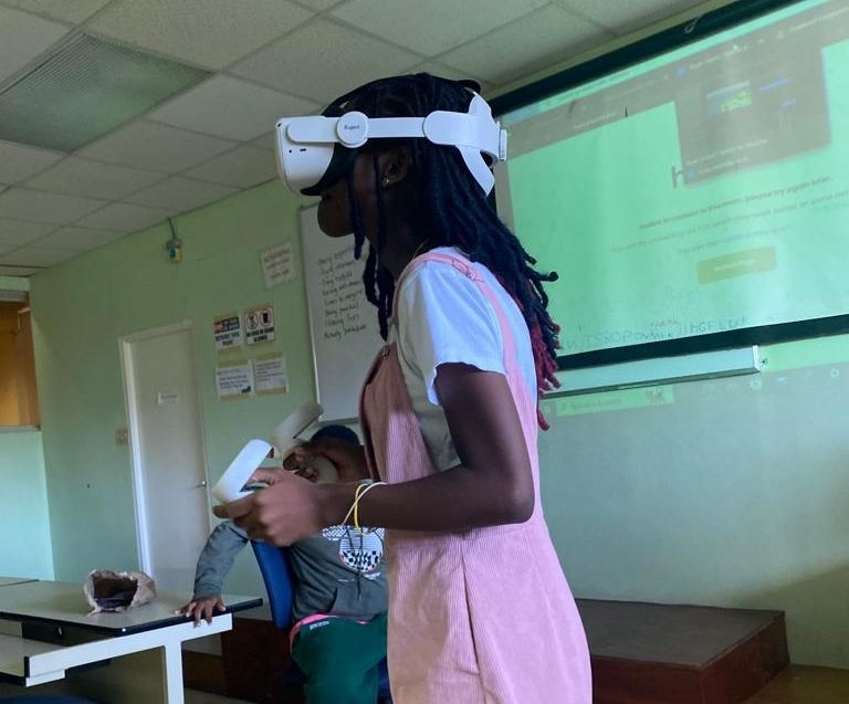 Girl in pink dress in classroom wearing white VR goggles