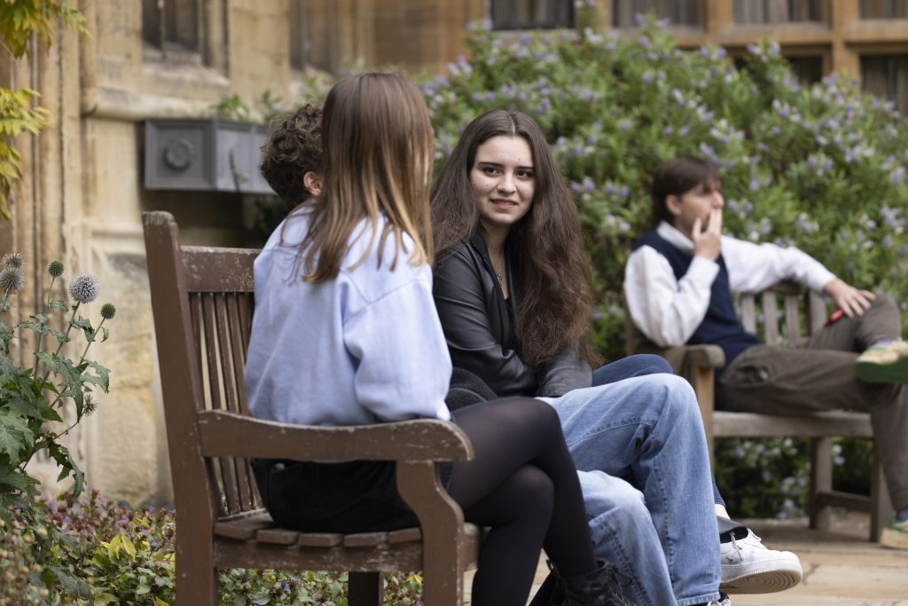 Three students sit on a bench chatting