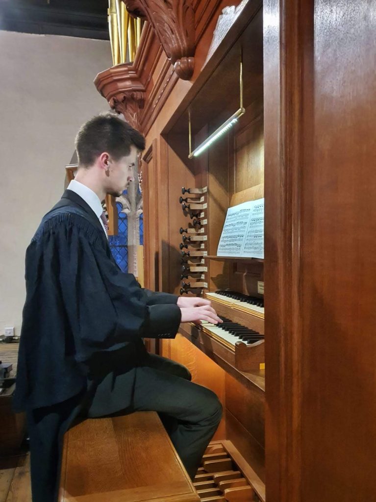 Man sits on stool in front of organ with hands on keyboard
