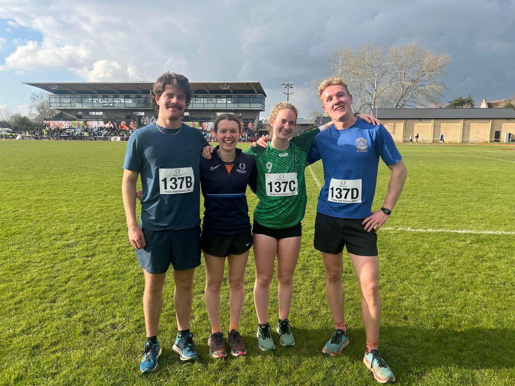 4 people in running clothes standing on the grass of a sports track