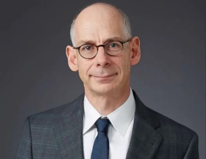 White male with grey hair and glasses wearing suit