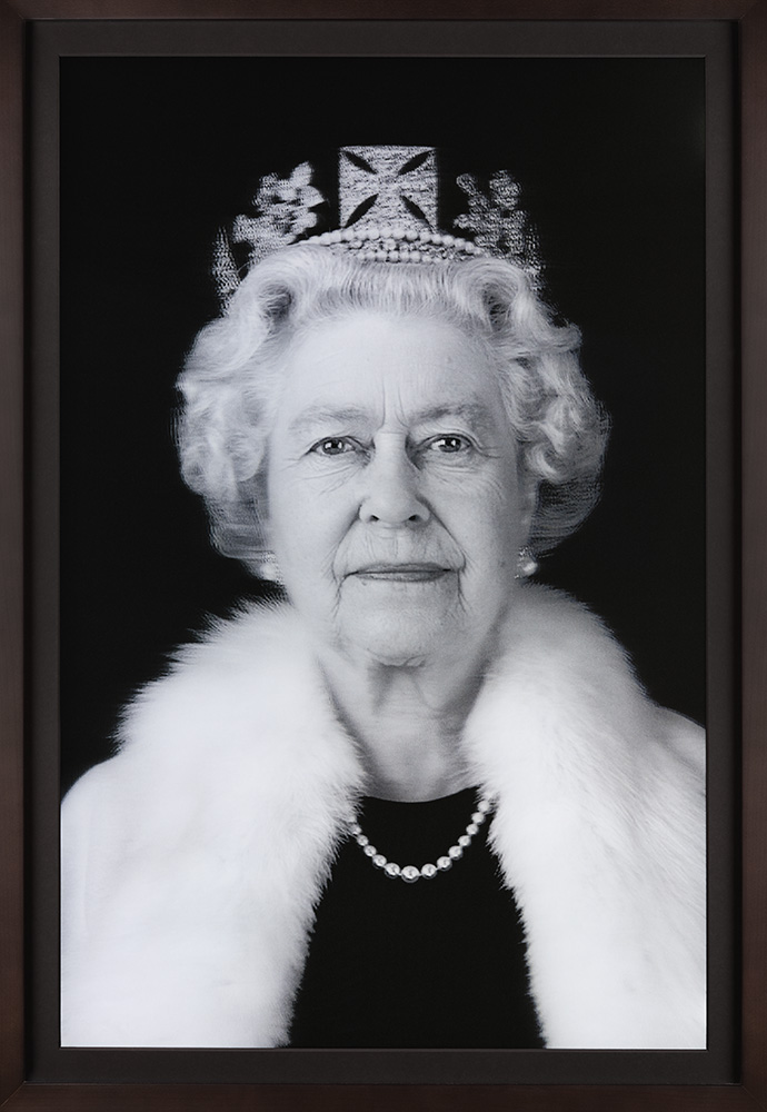 black and white image of the late Queen wearing a fur stole and crown, gazing directly out at audience.