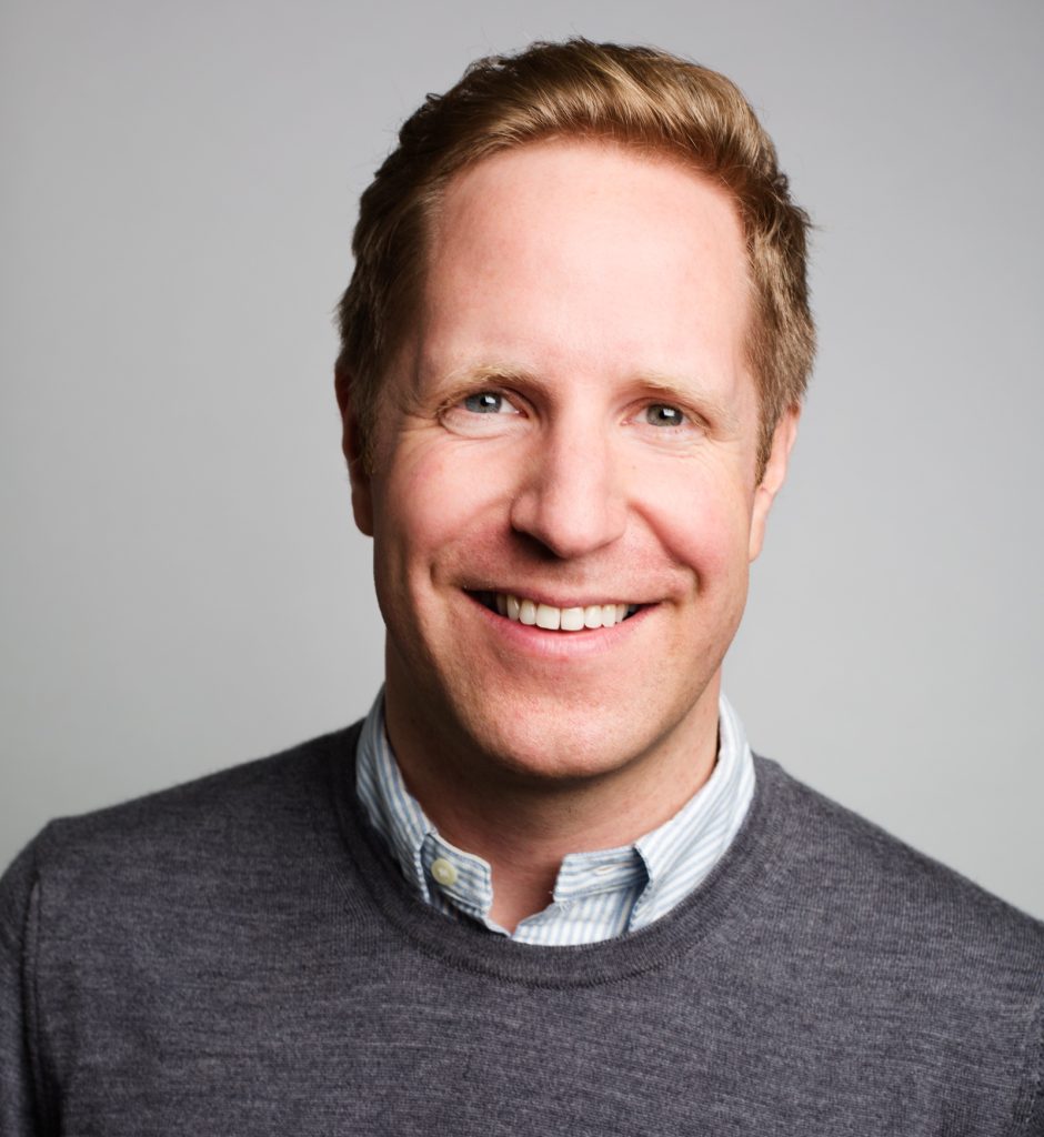 White male with sandy hair wearing grey jumper over blue shirt
