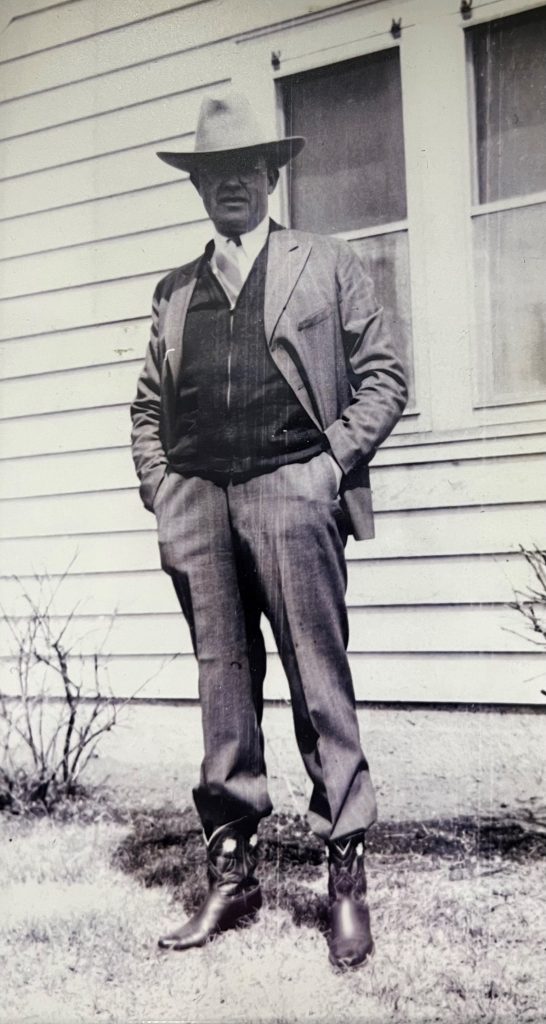 B&W photo os tall man wearing glasses, a cowboy hat and cowboy boots