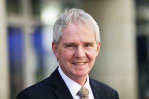 Head shot of man with white hair smiling at camera.
