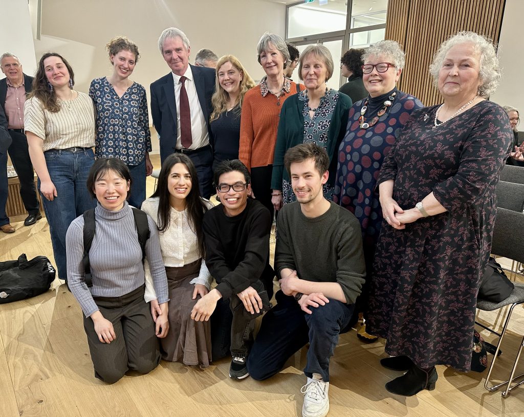 A group of men and women in two rows (one row kneeling) smile at camera.